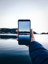 Cropped hand photographing lake through mobile phone