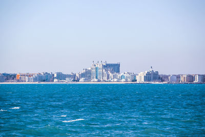 Sea and buildings in city against clear sky