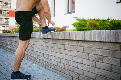 Low section of shirtless man tying shoelace on retaining wall