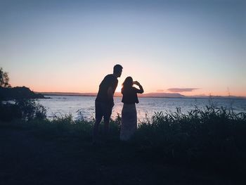 Silhouette couple standing at beach against clear sky during sunset