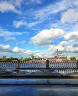 Bridge over river by buildings against sky