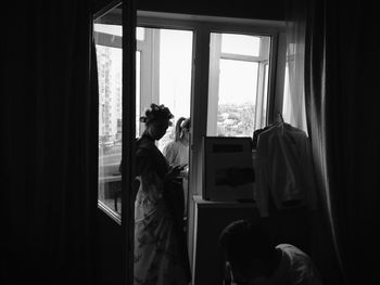 Rear view of man looking through window at home