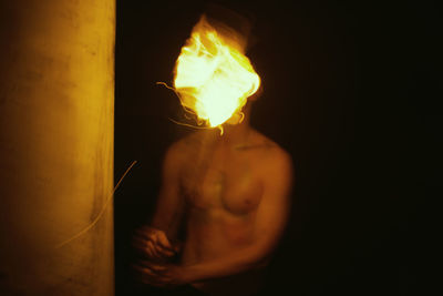 Midsection of shirtless man holding fire against black background