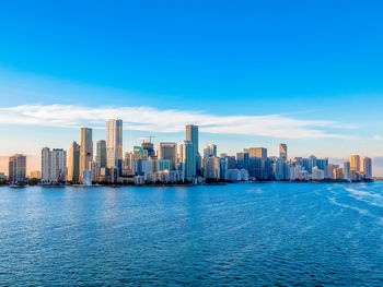 Sea by buildings in city against blue sky