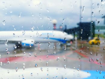 Airplane on runway against sky seen from wet window