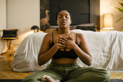 Woman meditating on exercise mat in bedroom at home