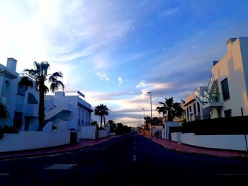 Road amidst buildings against sky during sunset