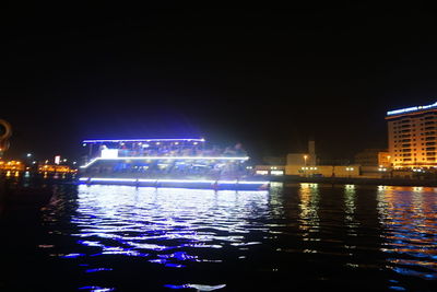 Illuminated buildings by river against sky at night