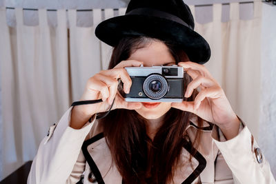 Woman photographing through vintage camera against curtains