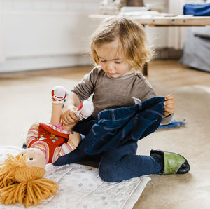 Cute girl playing with doll while sitting at home