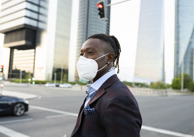 Side view of determined african american male entrepreneur in protective mask in downtown during coronavirus outbreak looking away
