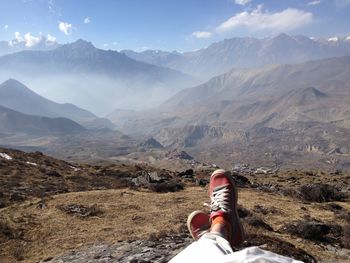 Low section of person sitting on mountain against sky