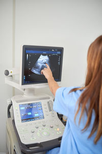 Back view of crop unrecognizable doctor showing video on ultrasound machine display during sonography diagnostic to patient