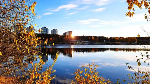 Scenic view of lake by buildings against sky during sunset