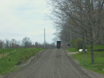 Road amidst bare trees against sky