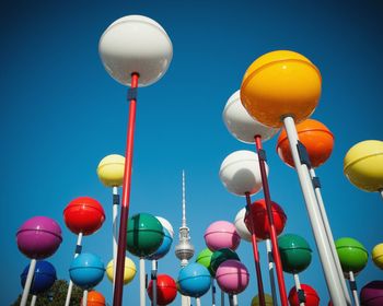 Low angle view of colorful spheres on poles against clear blue sky in city