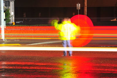 Rear view of light trails walking on illuminated colorful lights at night