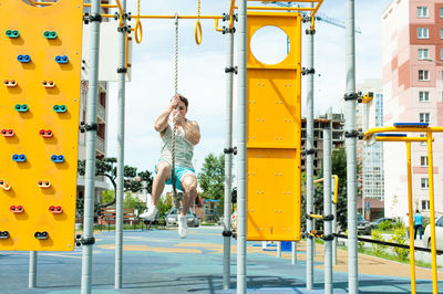 Young man hanging on rope against sky