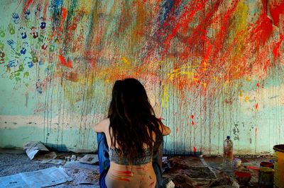 Rear view of woman sitting on floor against messy wall