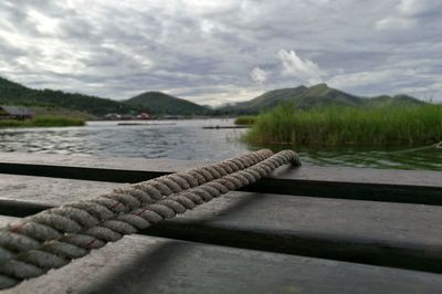 Close-up of rope on jetty in river against cloudy sky