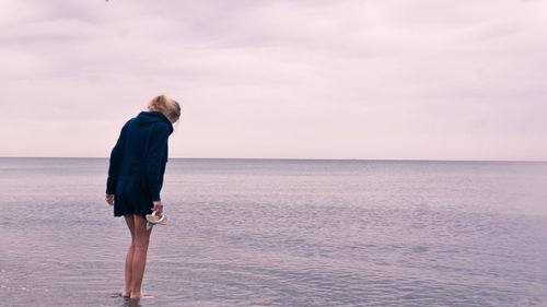 Full length of woman standing in water at beach against cloudy sky