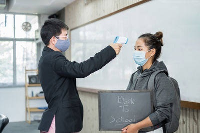 Side view of teacher checking temperature of student in classroom