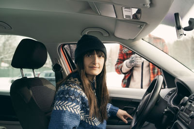 Portrait of woman sitting in car with friends standing at park