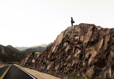 Low angle view of man standing on rock formation against clear sky