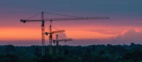 Silhouette cranes against sky during sunset