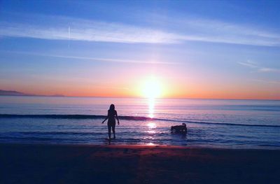 Silhouette woman on beach against sky during sunset