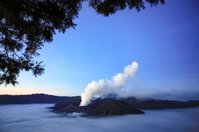 Smoke emitting from volcanic mountain against blue sky