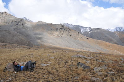 Man relaxing on mountain against cloudy sky