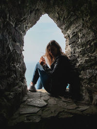 Portrait of woman sitting in rocky window  by sea