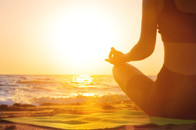 Rear view of woman with arms raised against sea during sunset