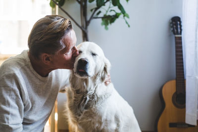 Loving senior man kissing affectionate dog at home