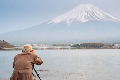 Rear view of senior man photographing by lake 