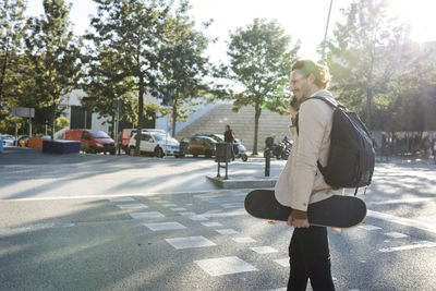 Man on the phone with backpack and skateboard crossing the street