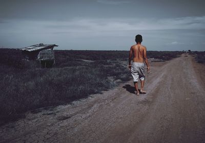 Rear view of man walking on road against sky