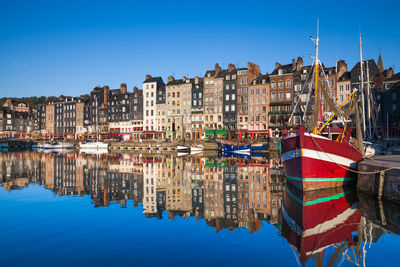 Reflection of buildings on water in city against clear blue sky