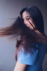 Beautiful young woman with tousled hair against gray wall