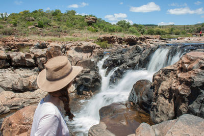 Rear view of man standing on rock against waterfall