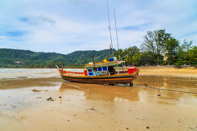 Boat moored on beach against sky