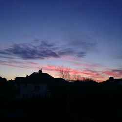 Silhouette houses against dramatic sky during sunset