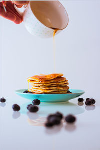 Cropped hand of person pouring honey on stacked pancakes against white background