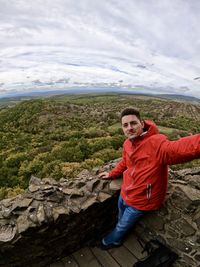 Portrait of young man sitting on rock against sky