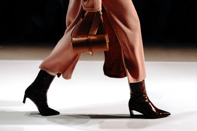Small leather handbag in woman's hand, a long dress and high-heeled boots. women's stylish  fashion