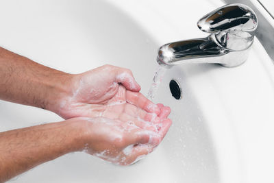 High angle view of woman drinking water from faucet in bathroom