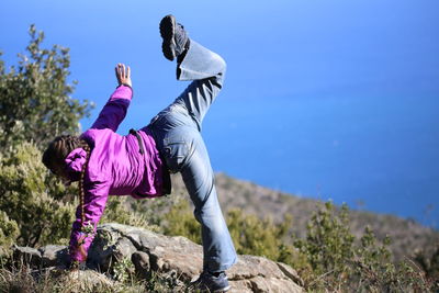 Woman exercising on rock against clear blue sky