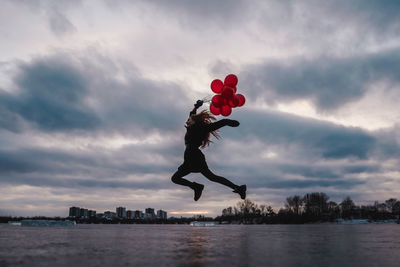 Man jumping on red balloon against sky