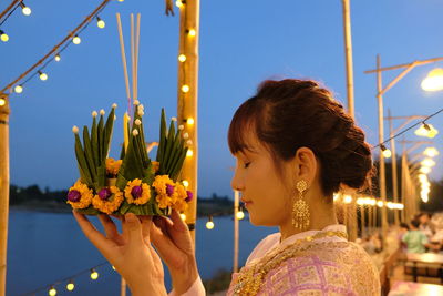 Woman holding flower decoration at lakeshore against sky